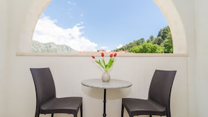 En balkon med to fletstole og et rundt bord med en vase røde blomster.