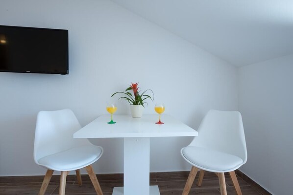 Una habitación moderna con una mesa blanca, dos sillas blancas, una planta en maceta y dos vasos de jugo de naranja.