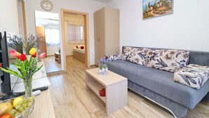 A living room with a grey sofa, a wooden coffee table, a vase with flowers, a bowl of fruit, and a painting on the wall.