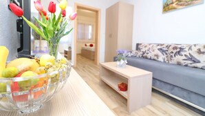 A living room with a sofa, a coffee table, and a bowl of fruit and flowers on a wooden table.