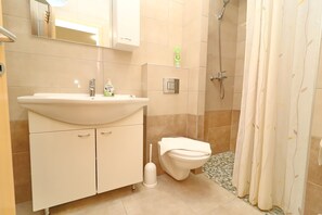 A bathroom with a sink, toilet, shower, and a mirror.