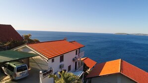 A coastal building with a red tiled roof, a parked van, and a view of the sea.