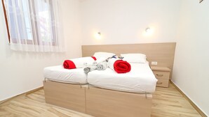 A double bed with white bedding and red accents, a wooden headboard, bedside tables, and a window with sheer curtains.