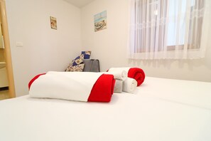 A neatly made bed with red and white bedding, a suitcase, and a jacket on the floor.