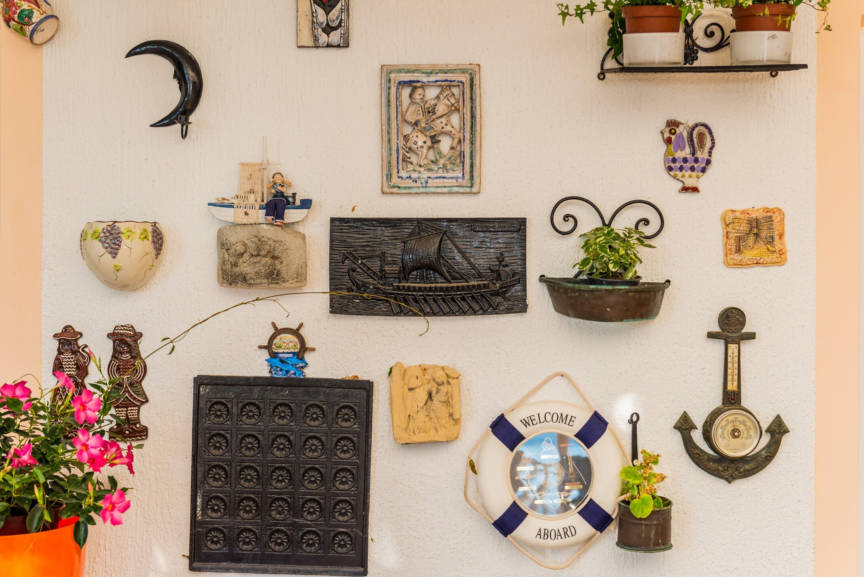 A wall decorated with various items including a crescent moon, a ship, a life preserver, and several potted plants.