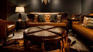 A room with a tufted headboard sofa, a round leather ottoman, a lamp, and a wall-mounted bull skull. - The Barfield, Autograph Collection (Amarillo)