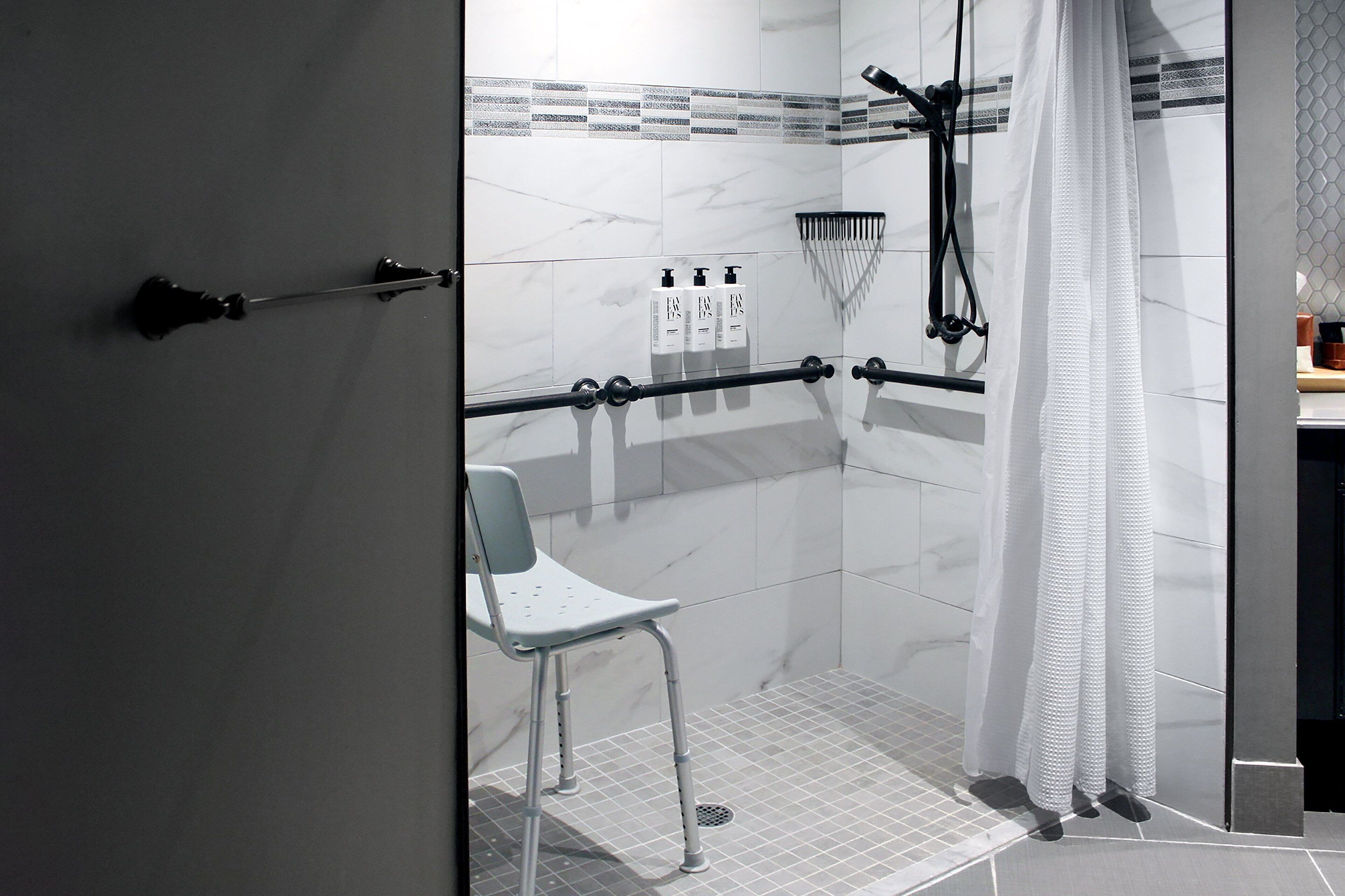 Un bagno moderno con cabina doccia in vetro, una sedia bianca e un porta asciugamani.