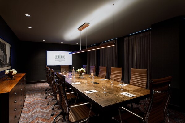 A conference room with a long wooden table, leather chairs, and a projector screen displaying a presentation.