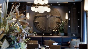 A modern restaurant interior with a central seating area, a decorative wall with a large circular emblem, and a chandelier. - The Barfield, Autograph Collection (Amarillo)