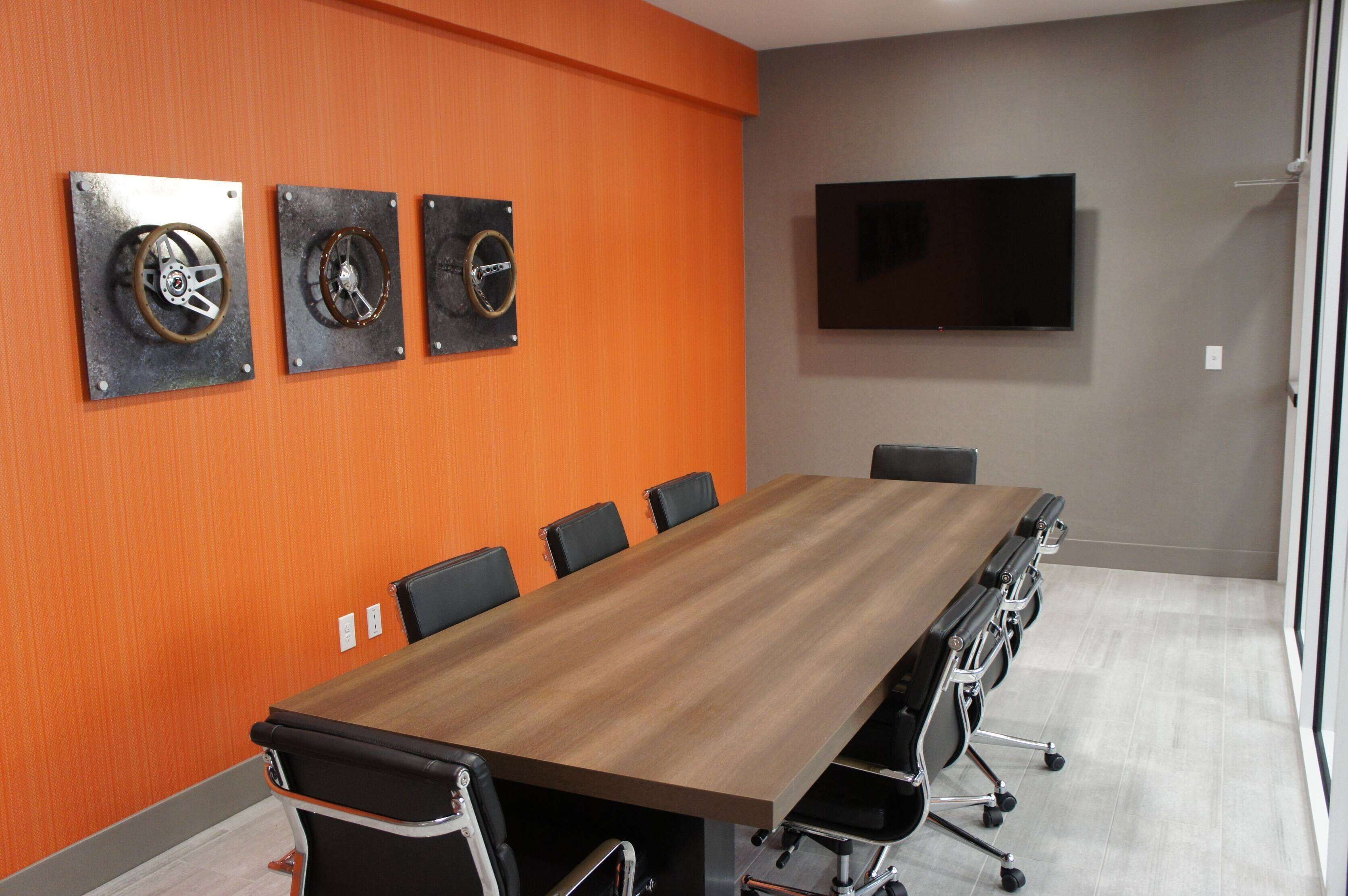 Un salón de conferencias con una larga mesa, seis sillas y tres altavoces instalados en la pared.