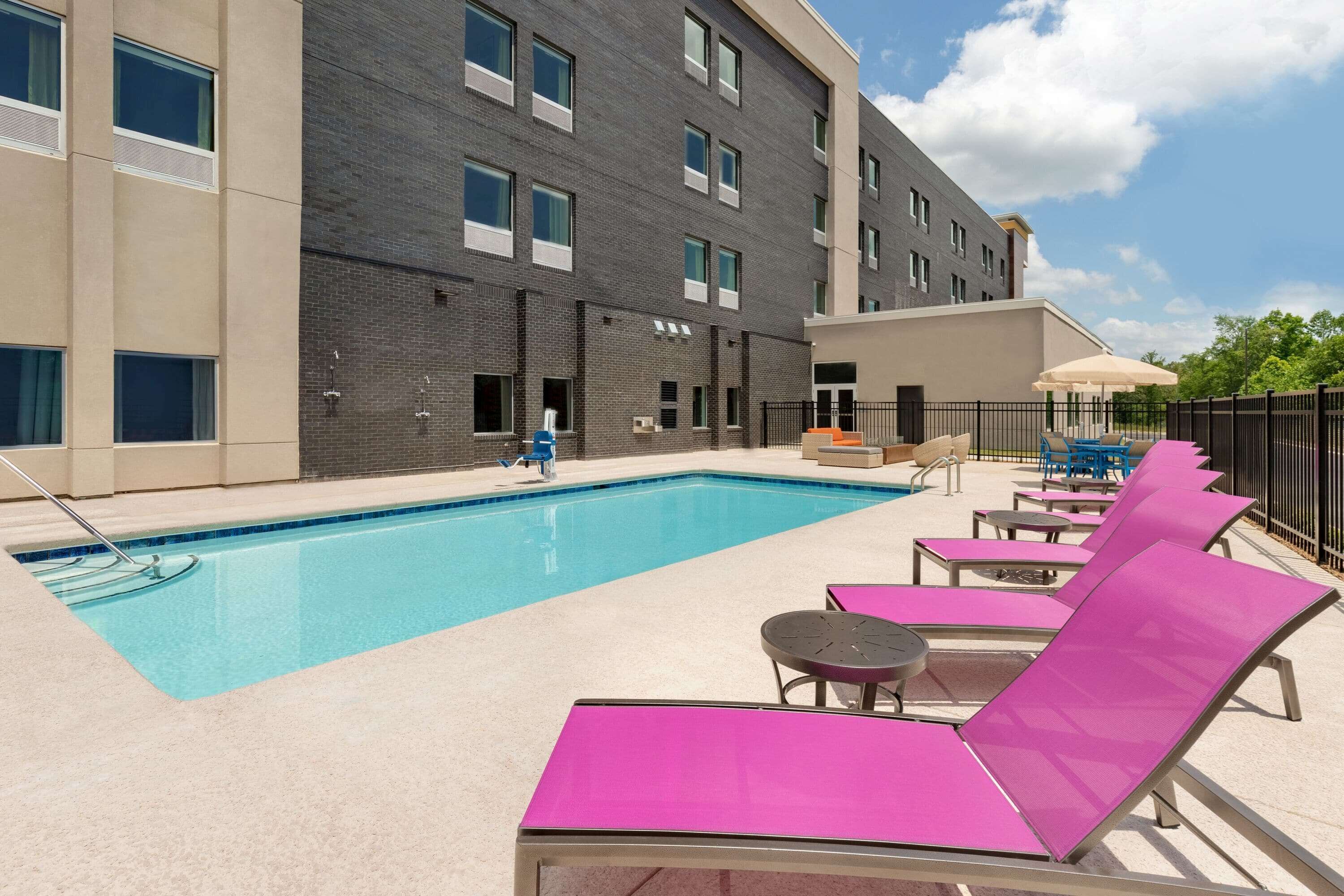 A swimming pool with lounge chairs and a building with multiple windows and a brick facade.