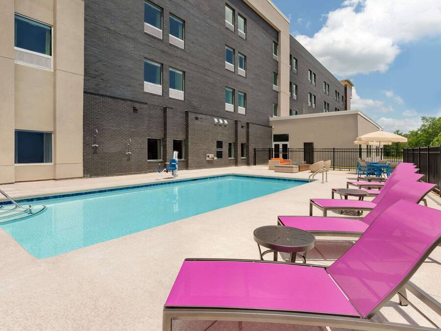 A swimming pool with lounge chairs and a building with multiple windows and a brick facade.