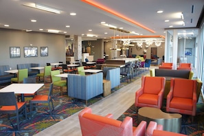 Um hall de hotel moderno com várias áreas de estar, incluindo cabines e mesas, e um bar central.