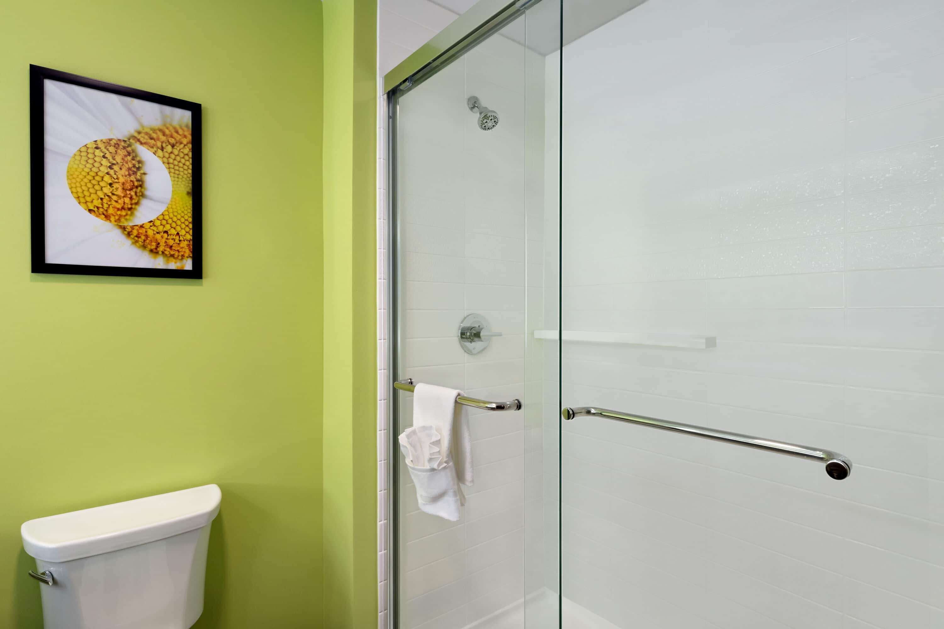 Et badeværelse med en glas brusekabine, et hvidt toilet og et billede i ramme på væggen.