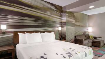 Habitación de hotel con una cama grande, un sofá, una mesita de noche y una pared con un mural texturizado.