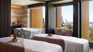 A hotel room with two beds, a marble bathtub, and a city view.