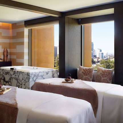 A hotel room with two beds, a marble bathtub, and a city view.
