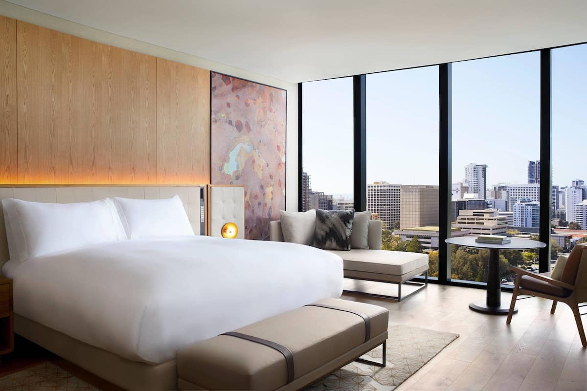 Una habitación de hotel moderna con una cama grande, un espacio de descanso con vistas a la ciudad y una mesita.