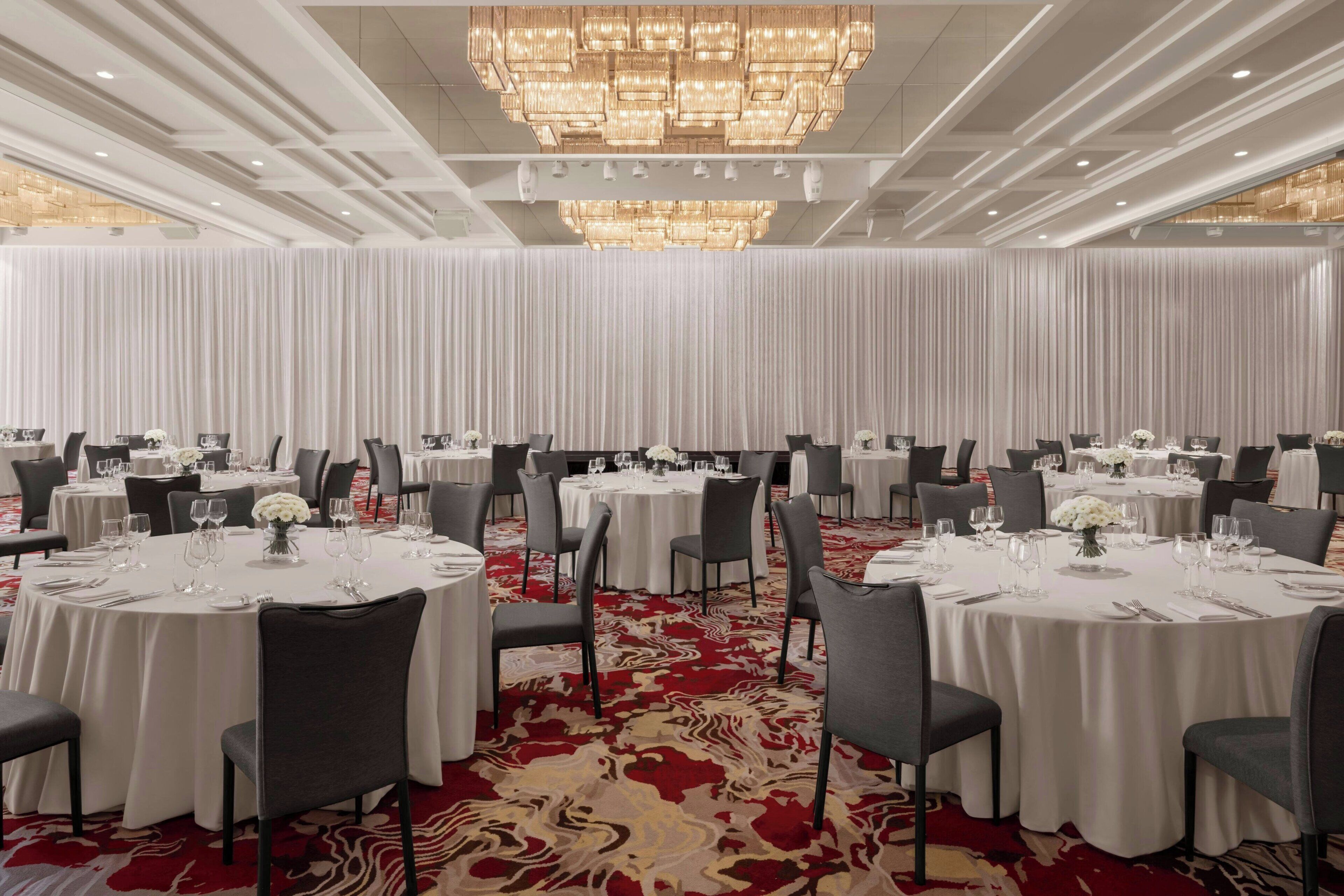 A banquet hall with round tables, chairs, and a red carpet.