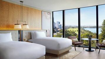 Een moderne hotelkamer met twee bedden, een eettafel en uitzicht op een stadsbeeld en water.