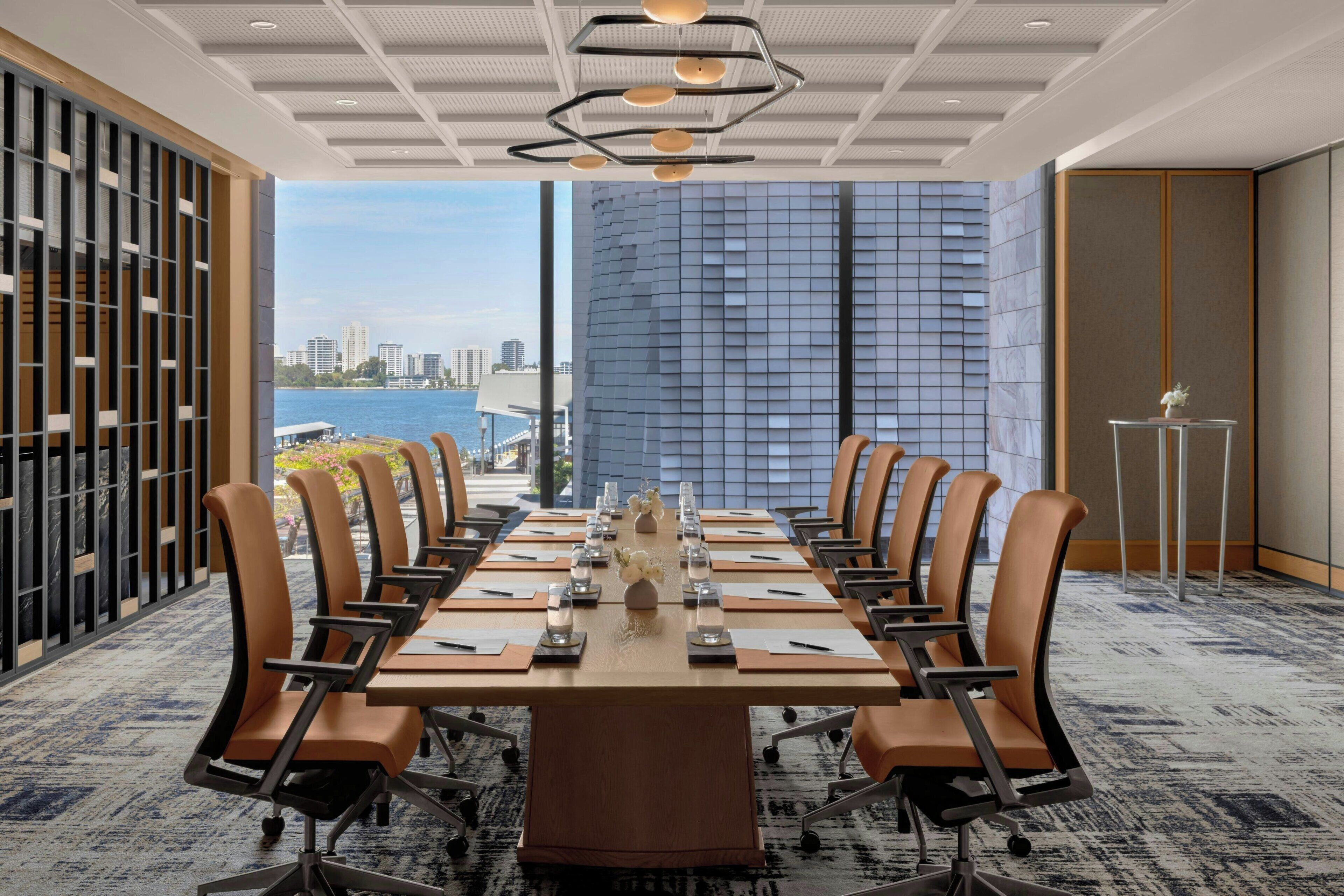 A conference room with a long table, chairs, and a view of a cityscape and water.