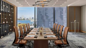 A conference room with a long table, chairs, and a view of a cityscape and water.
