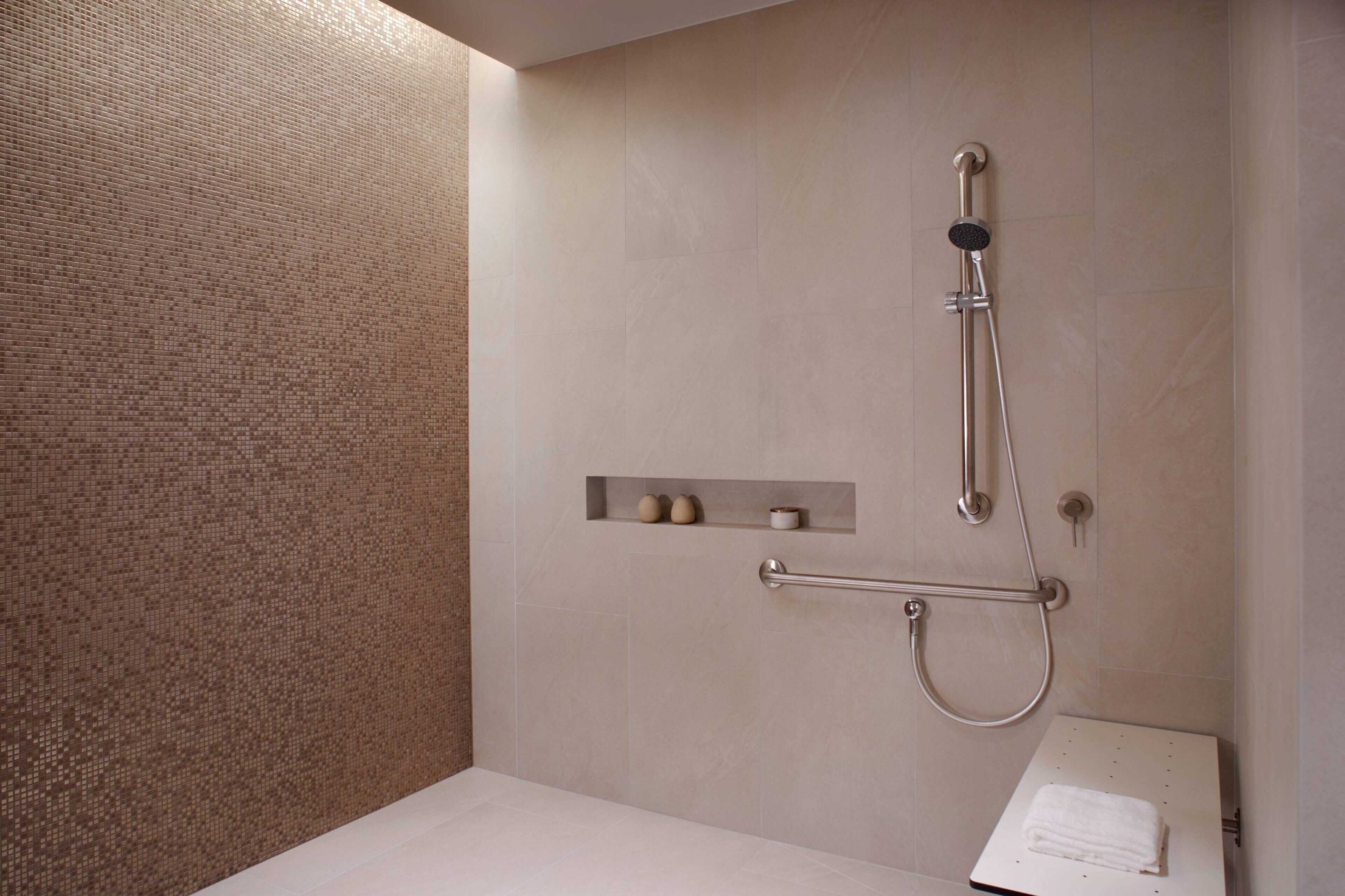 A modern bathroom with a shower, a handrail, and a shelf with toiletries.