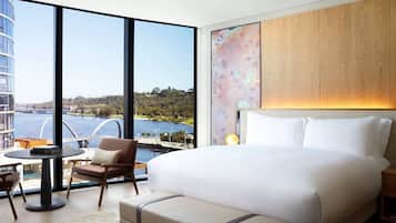 Una habitación de hotel moderna con una cama grande, vista a un cuerpo de agua, un panel de pared de madera y una zona de estar con una mesa y sillas.