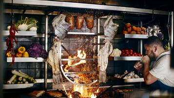 Una cocina con un asador, estantes con verduras y una persona cuidando el fuego.