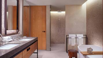 Un baño moderno con dos lavamanos, un espejo grande, una puerta de madera, un box de ducha con paredes de vidrio y una bañera con un taburete de madera.