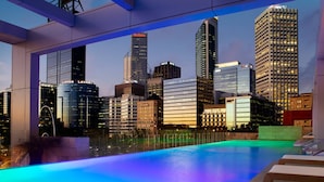 An infinity pool with a city skyline view, modern architecture, and a well-lit pool area.