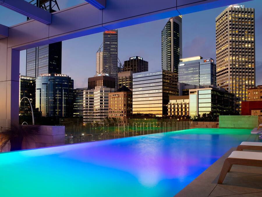 Una piscina infinita con vistas al horizonte urbano, arquitectura moderna y un área de piscina bien iluminada.