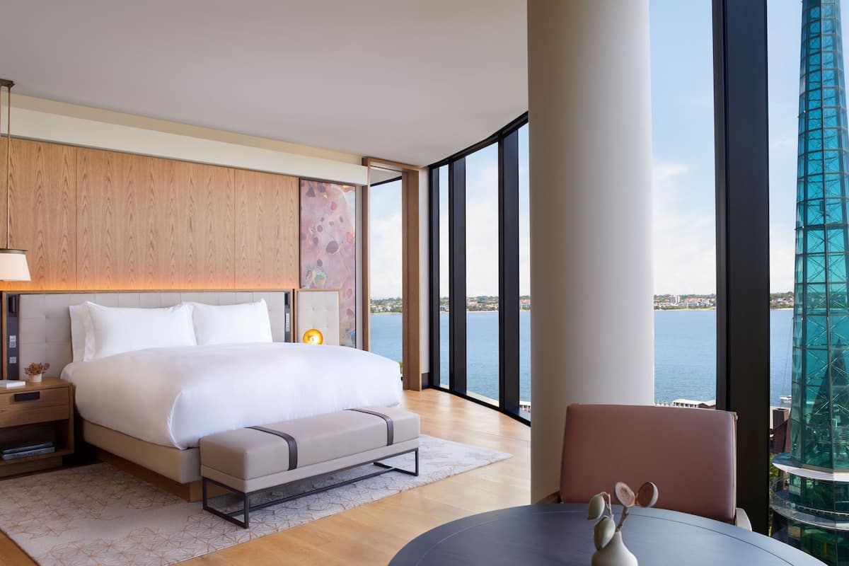 Habitación de hotel moderna con una cama grande, una mesita de noche, una silla y vistas a la ciudad y al agua.