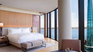 A modern hotel room with a large bed, a bedside table, a chair, and a view of the city and water.