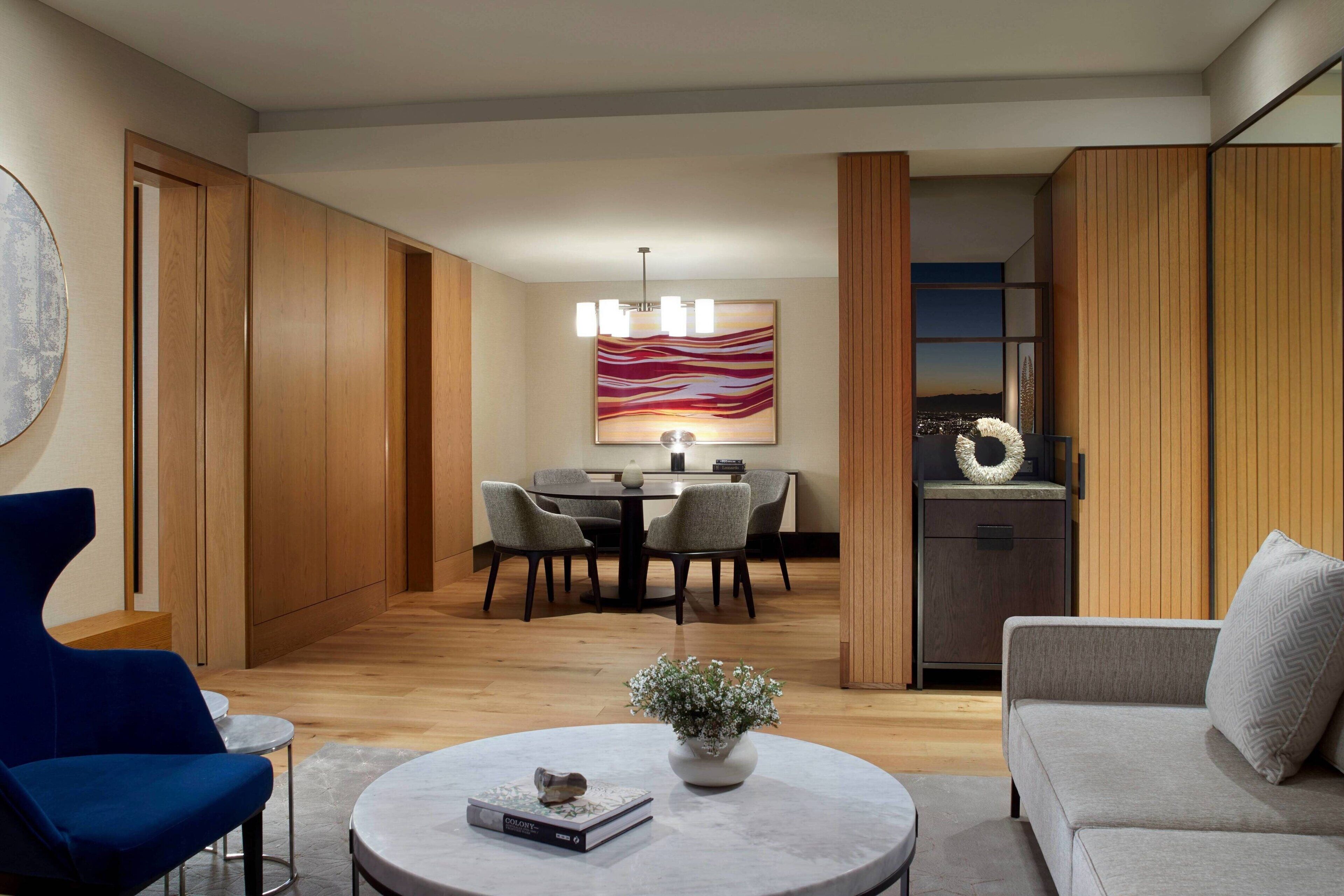 A modern living room with a round coffee table, a blue armchair, a grey sofa, and a dining area with a round table and chairs.