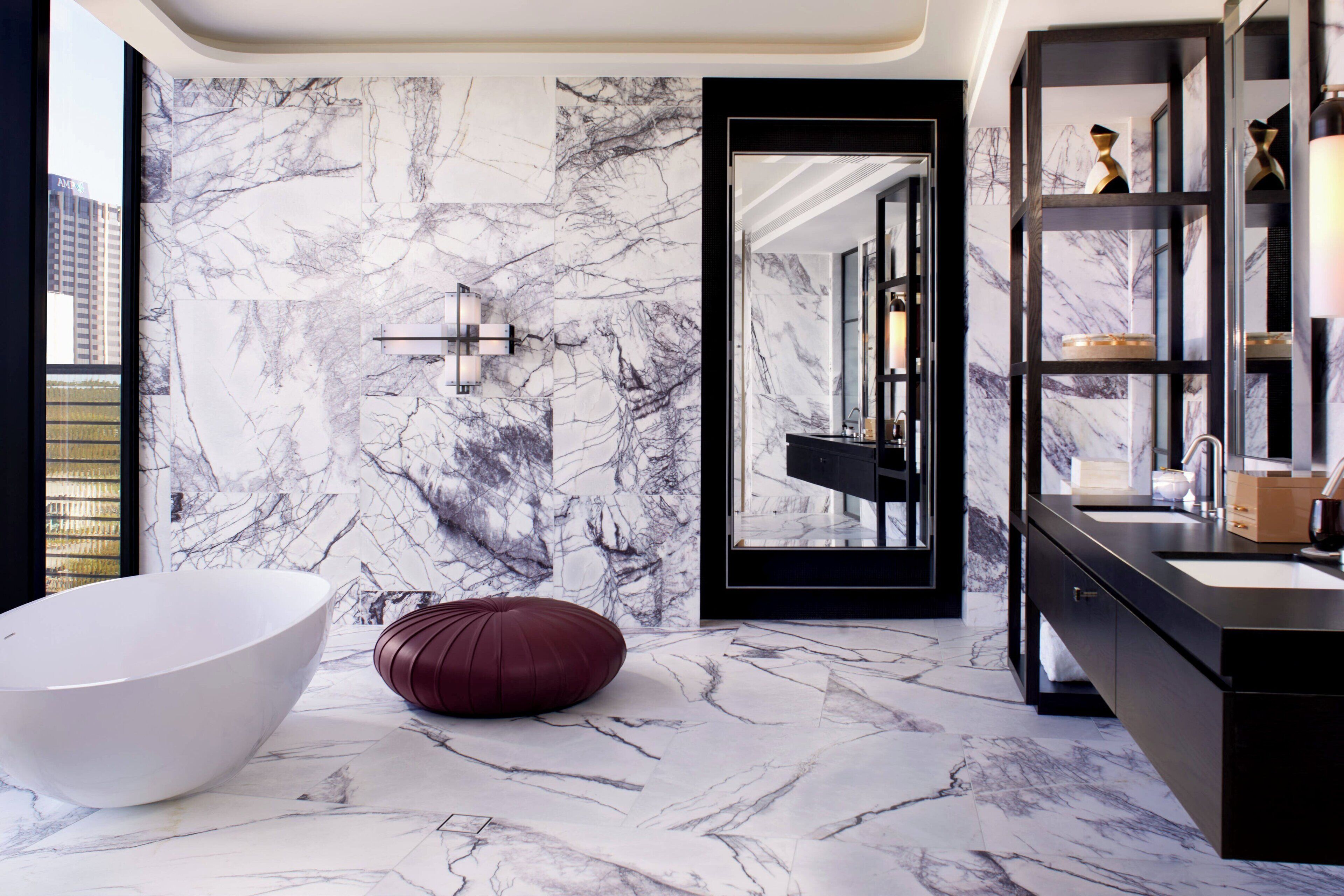 Un baño moderno con una bañera blanca grande, un pouf rojo y una pared de mármol.