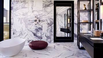 Un baño moderno con una bañera blanca grande, un pouf rojo y una pared de mármol.