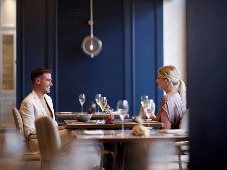 A dining area with a table set for two, a chandelier, and a wall-mounted light fixture.