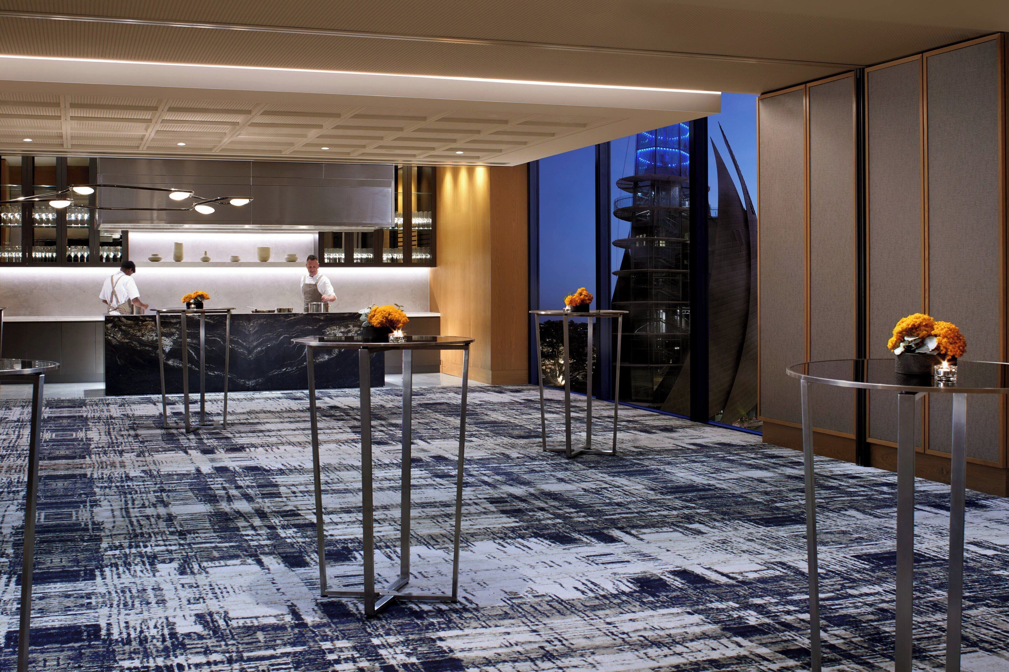 A modern hotel lobby with a marble reception desk, a bar area, and a seating area with round tables.