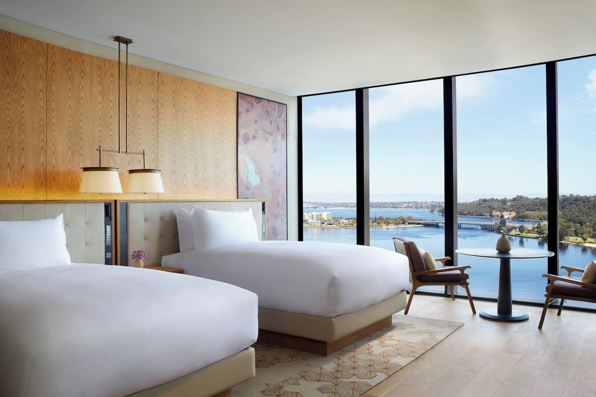 Una habitación de hotel moderna con dos camas, vista a un cuerpo de agua y un área de comedor con mesa y sillas.