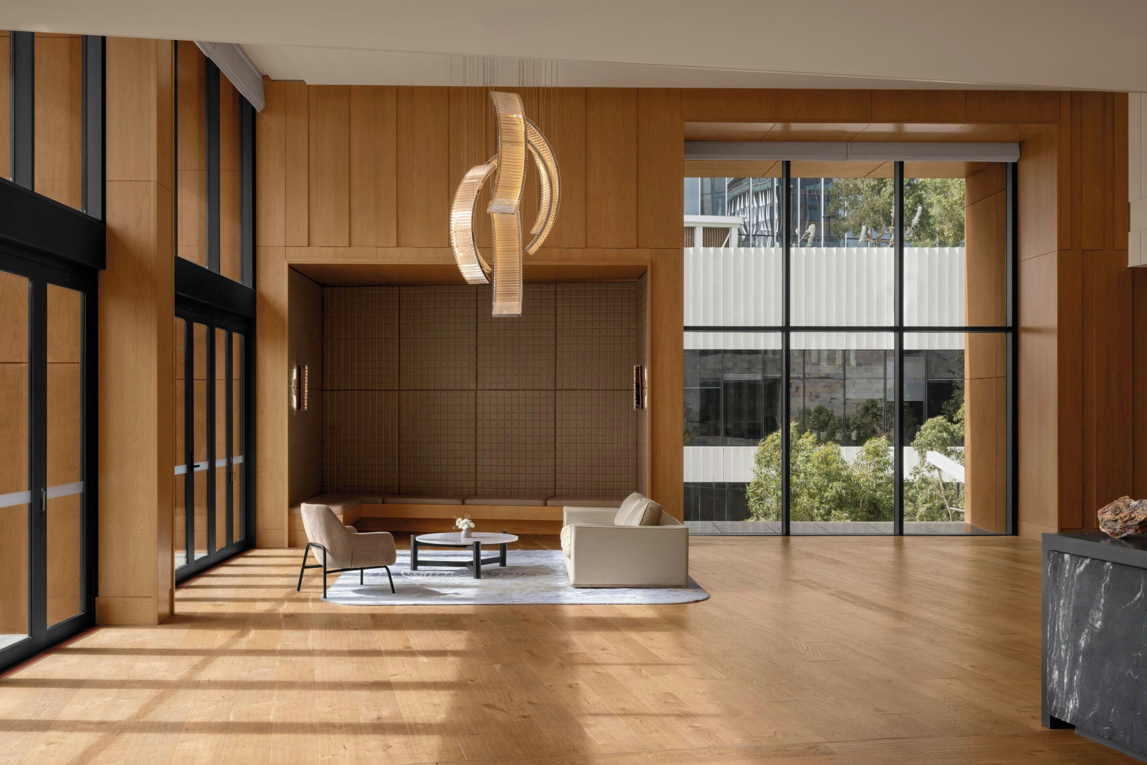 A spacious room with a wooden floor, a seating area with two sofas and a coffee table, a large window with a view, and a modern light fixture.