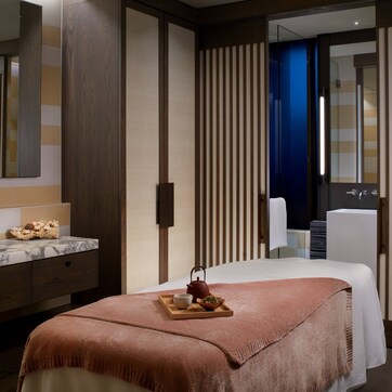 A modern hotel room with a marble bathroom sink, a large bed with a pink throw, and a tea set on a tray.