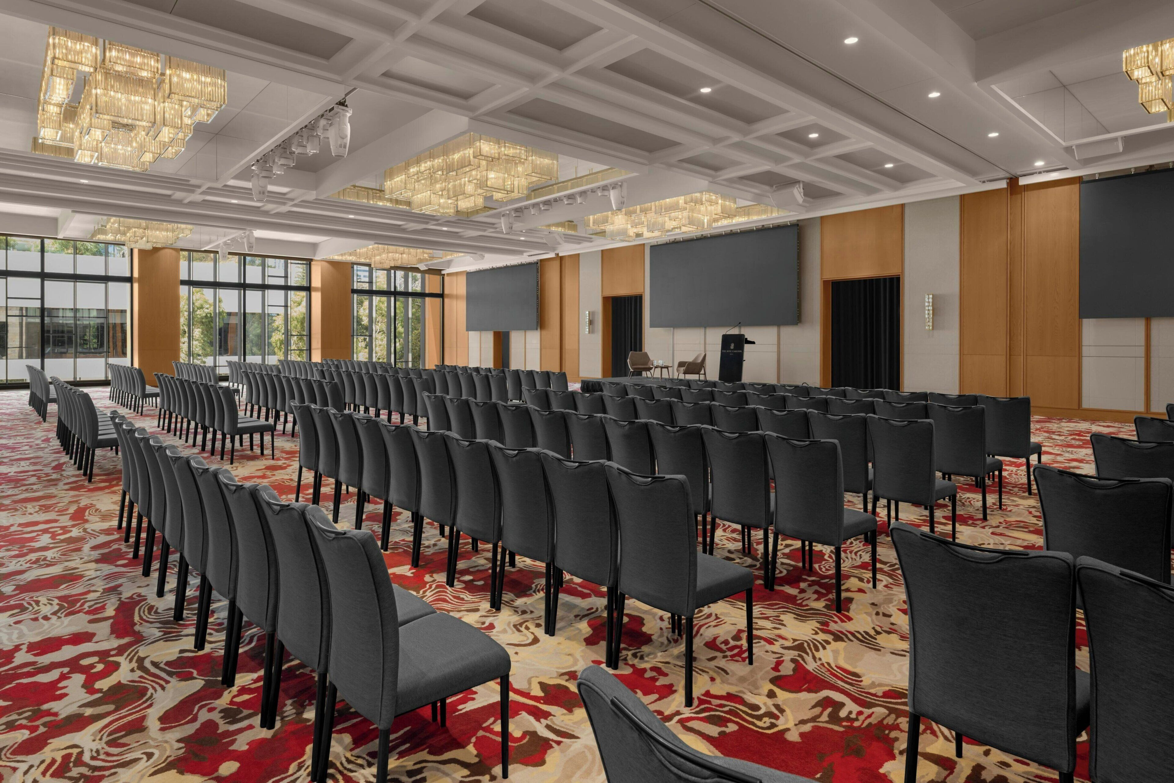 A conference room with rows of chairs, a large screen, and chandeliers.