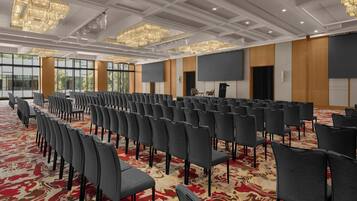 A conference room with rows of chairs, a large screen, and chandeliers.