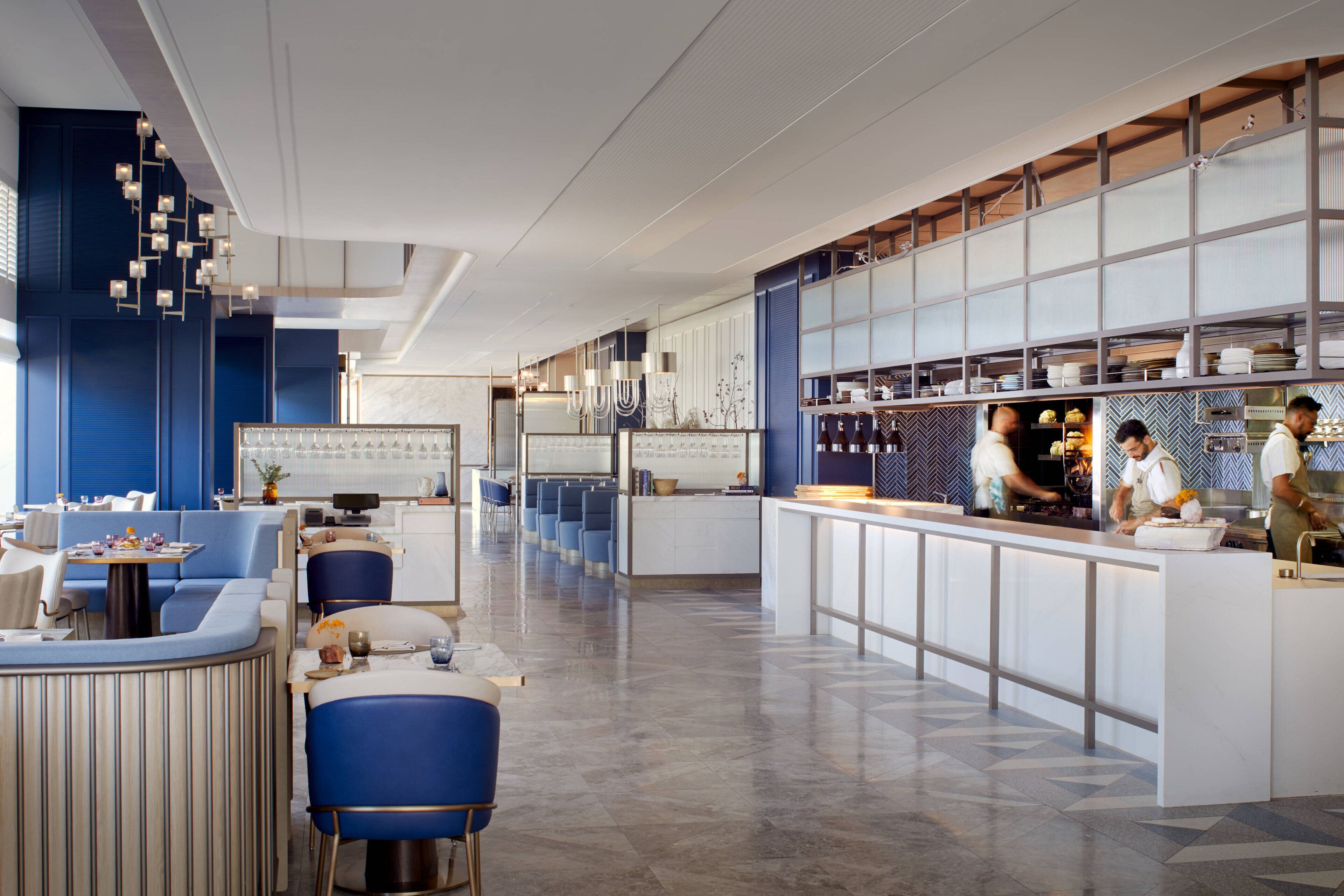 Un restaurante moderno con una barra alargada, asientos azules y una zona de cocina.