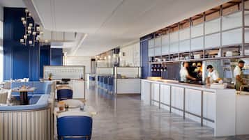 Un restaurante moderno con una barra alargada, asientos azules y una zona de cocina.