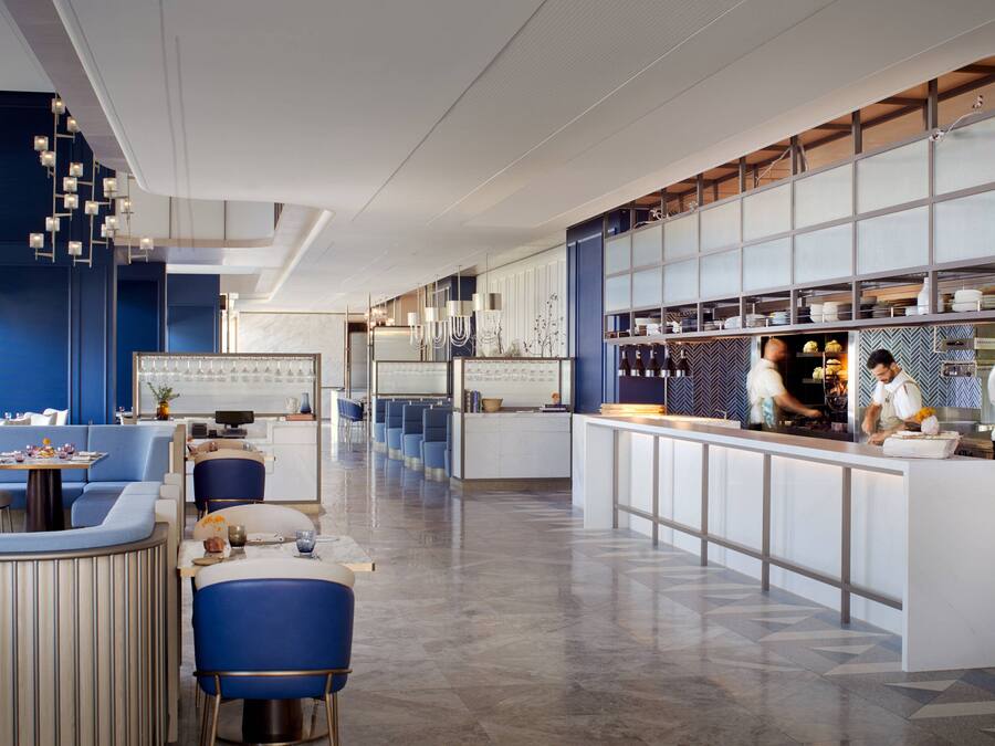 Un restaurante moderno con una barra alargada, asientos azules y una zona de cocina.