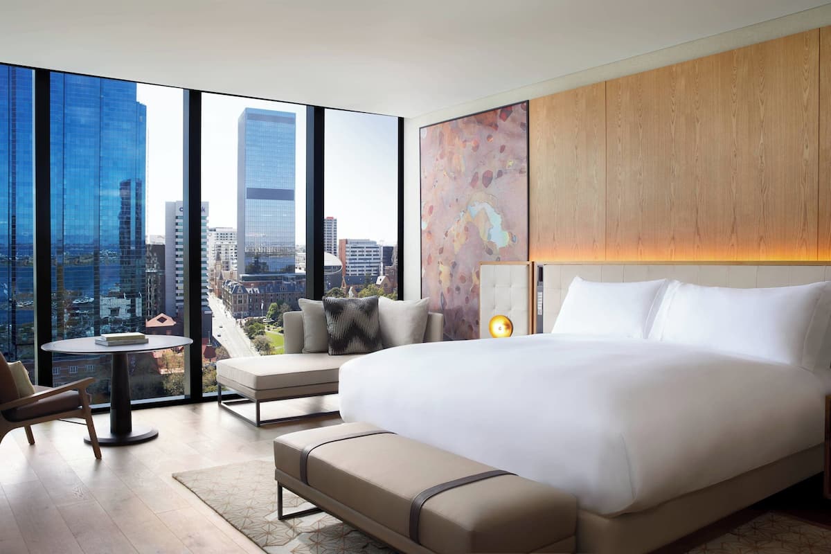 Una habitación de hotel moderna con una cama grande, un área de descanso y vistas de la ciudad a través de ventanas de piso a techo.