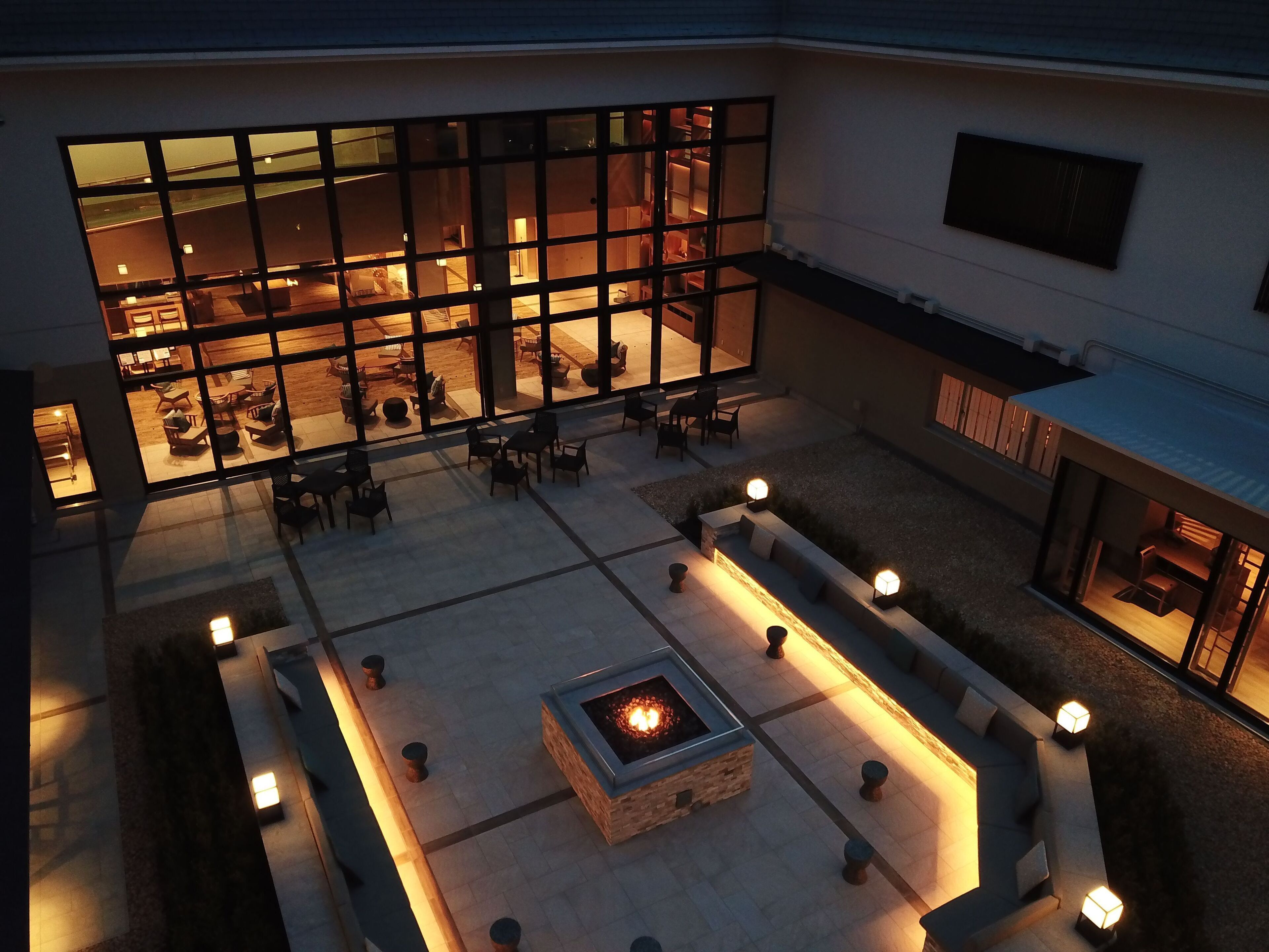 A courtyard with outdoor seating, a fire pit, and a building with large windows.