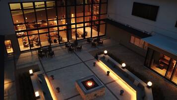 A courtyard with outdoor seating, a fire pit, and a building with large windows.